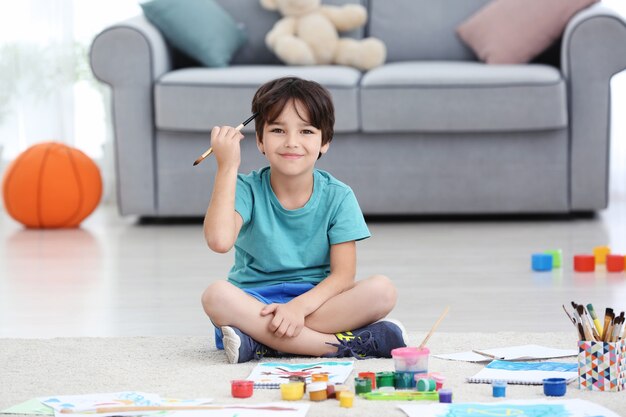 Little boy painting while sitting on floor indoors