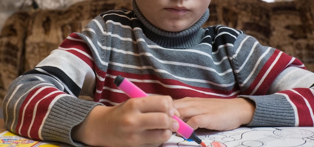 Un ragazzino dipinge una colorazione con pastelli e pennarelli su un tavolo di legno a casa.