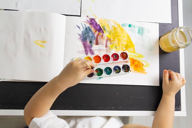 A little boy paints with watercolor paints on a table