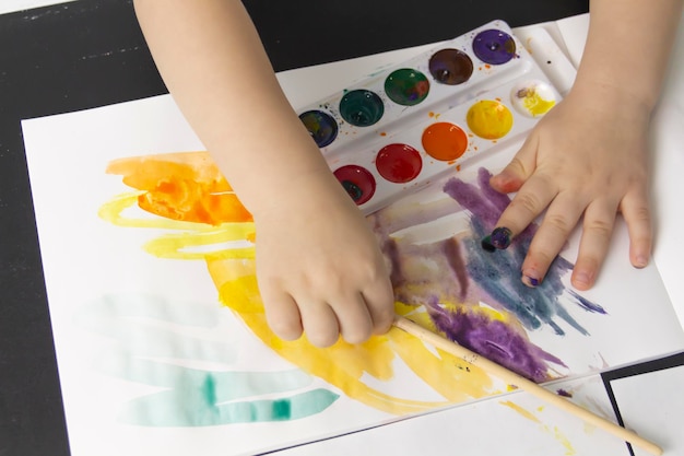 A little boy paints with watercolor paints on a table