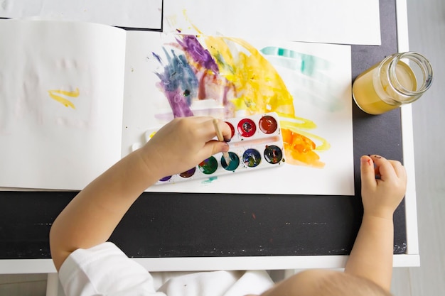 A little boy paints with watercolor paints on a table