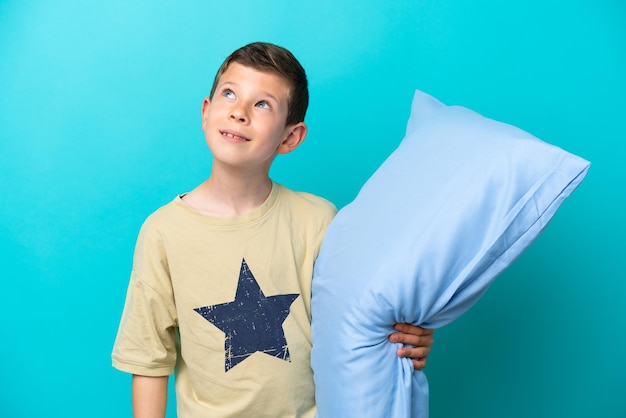 Little boy in pajamas isolated on blue background thinking an idea while looking up