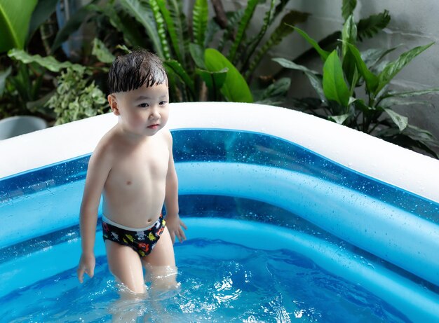 Little boy play in home water pool on garden summer day