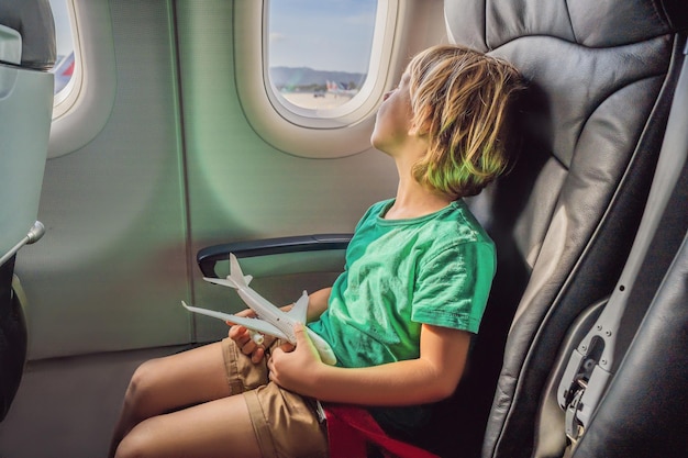 Маленький мальчик играет с игрушечным самолетом в коммерческом реактивном самолете, летящем в отпуск