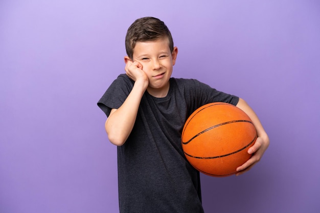 Маленький мальчик, играющий в баскетбол на фиолетовом фоне, разочарованный и закрывающий уши