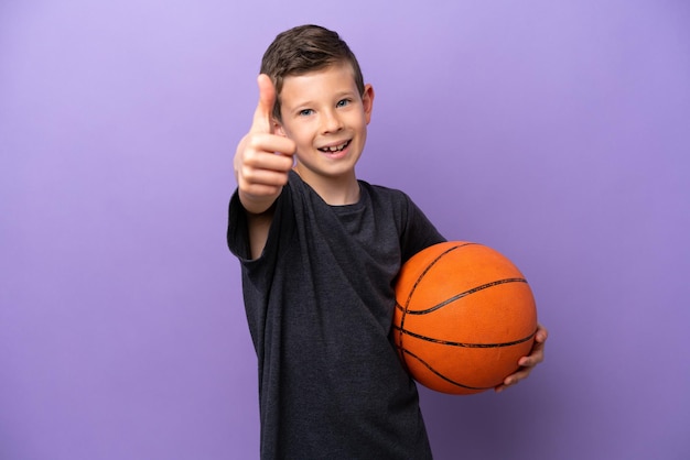 Маленький мальчик играет в баскетбол на фиолетовом фоне с поднятыми большими пальцами, потому что произошло что-то хорошее