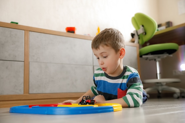 Little boy playing in the children's room lying on the floor with a typewriter and a high-speed track