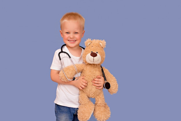 Little boy playing doctor and listening to a teddy bear with a stethoscope on a blue background