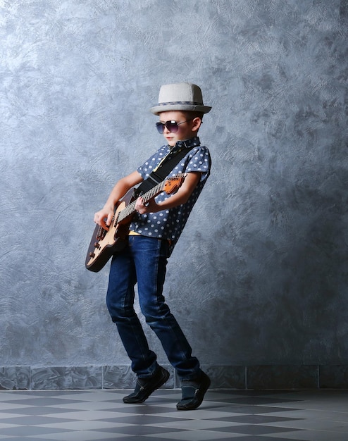 Little boy playing guitar on a grey wall background