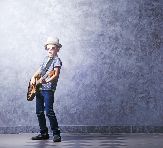 Little boy playing guitar on a grey wall background