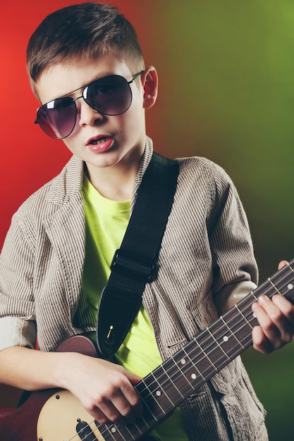 Фото Маленький мальчик играет на гитаре на ярком фоне