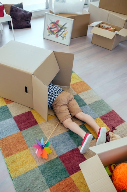 Little boy playing inside a moving box while his father unpacks in the living room