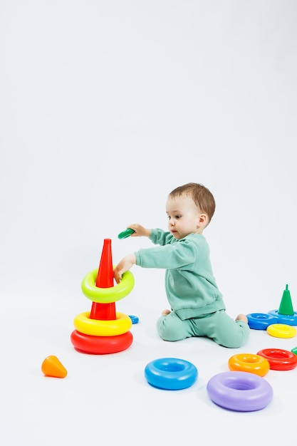 白い背景にプラスチック製のピラミッドでロジック教育ゲームをしている小さな男の子幸せな子供は教育玩具で遊んでいます赤ちゃんは 1 歳 4 ヶ月です