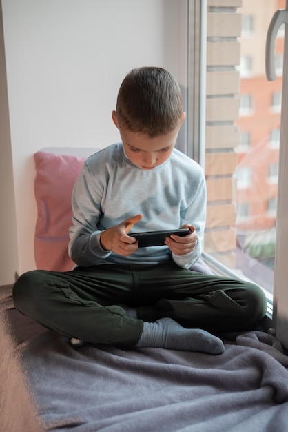 ソファの上に座ってスマートフォンでモバイルゲームをしている小さな男の子 家庭での子供のレジャービデオ