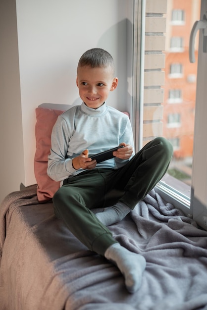 Little boy playing mobile game on smartphone sitting on a sofa\
top view child leisure at home video