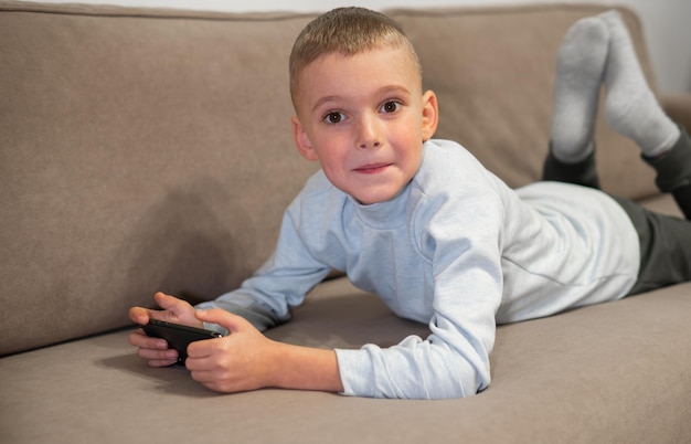 소파에 앉아 스마트폰으로 모바일 게임을 하는 어린 소년 가정 비디오에서 어린이 여가