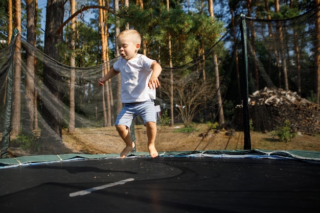 屋外で遊んでいる少年。芝生の上のトランポリンでジャンプする少年。フレンドリーな家族の概念。