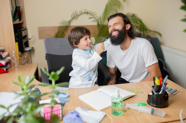 Little boy playing pretends like doctor examining a man in comfortabe medical office