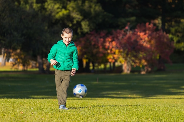 Little boy playing soccer with football on field in autumn park