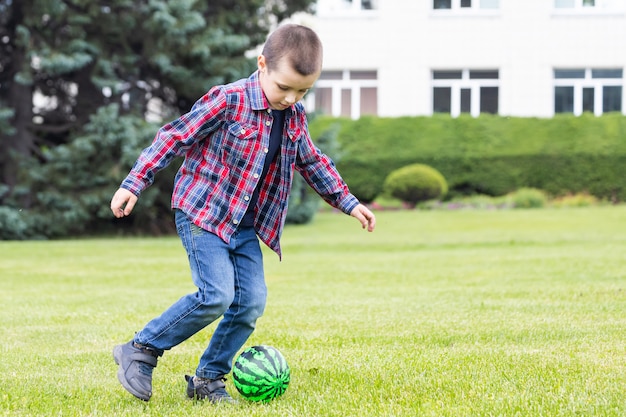 夏の公園のフィールドでサッカーとサッカーをしている少年。