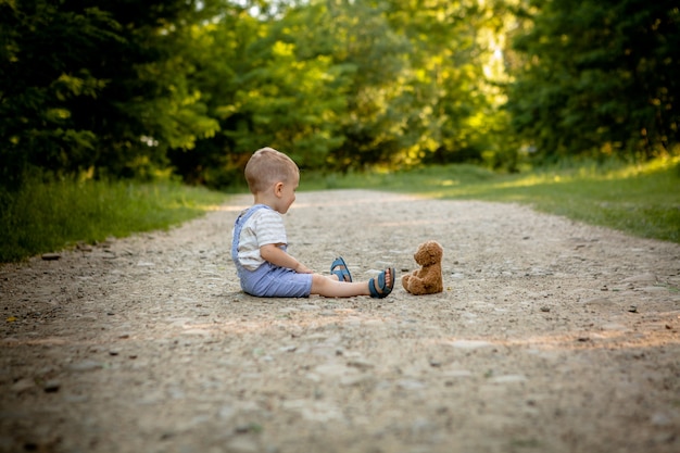歩道でテディベアと遊ぶ小さな男の子。