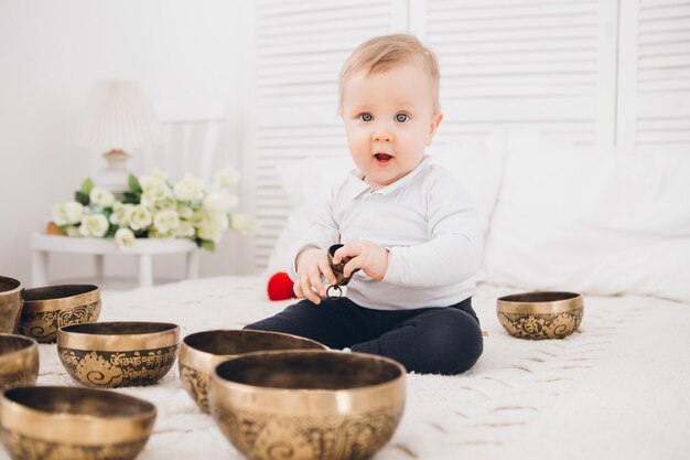 Little boy playing with Tibetan singing bowls sitting on the bed