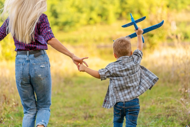 Ragazzino che gioca con l'aeroplano giocattolo con la sua giovane mamma all'aperto al tramonto. happy kid sta giocando nel parco all'aperto.