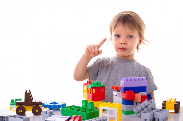 Little boy playing with toy blocks pointing his finger up, concentrated face isolated