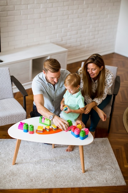 Маленький мальчик играет с игрушками в гостиной с отцом и матерью