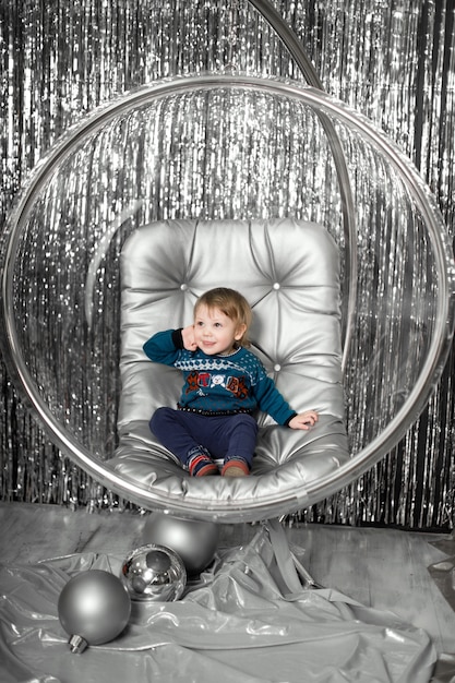 小さな男の子は椅子で銀のボールとガラスのボウルを果たしています。