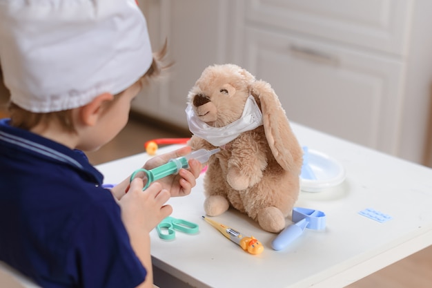 A little boy plays a doctor and injects a toy with a hare so that he can recover from the coronavirus COVID-19