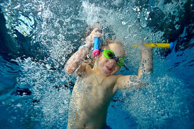 A little boy plays and swims underwater in the pool with toys in his hands in bubbles