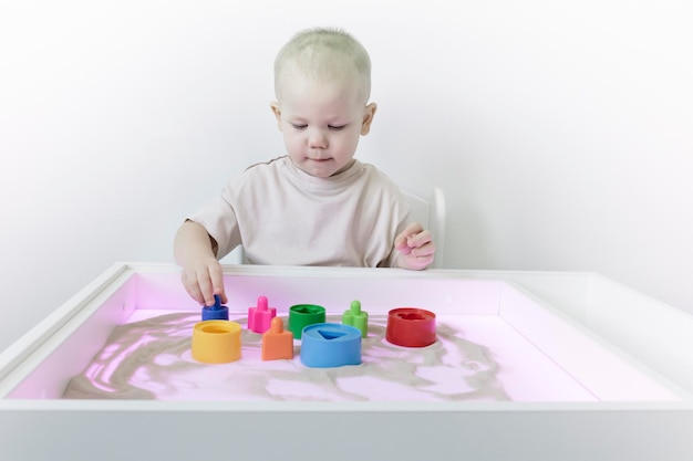 A little boy plays with sand shapes and a pyramid on a table with a purple subshirt