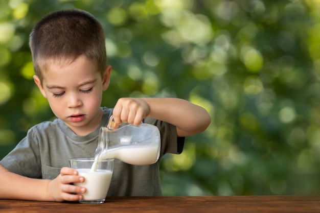 Photo little boy pouring milk into glass outdoors