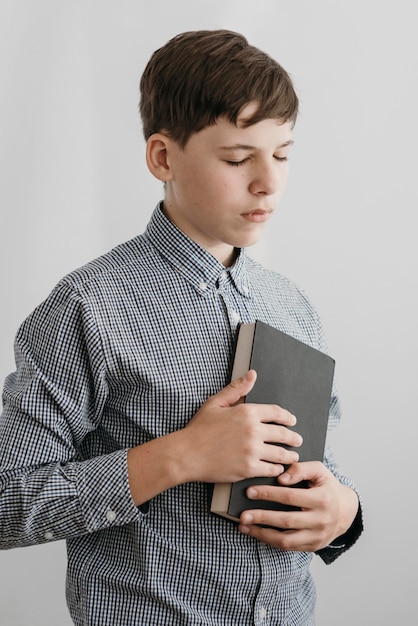 Little boy praying while holding a holy book