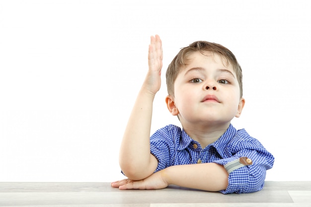 Маленький мальчик дошкольного возраста поднимает руку, чтобы ответить на вопрос