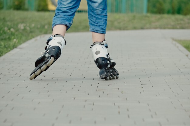 Little boy in protective equipment and rollers stands on walkway in park, low angle view