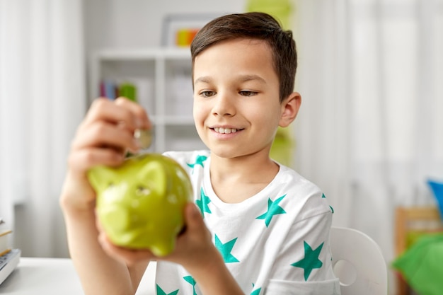 little boy putting coin into piggy bank at home