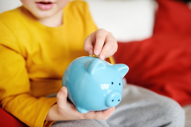 Little boy putting coin into piggy bank