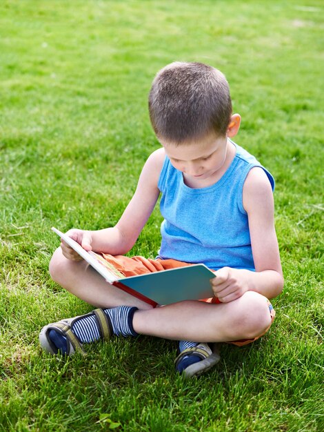 Little boy reading book outdoori on grass