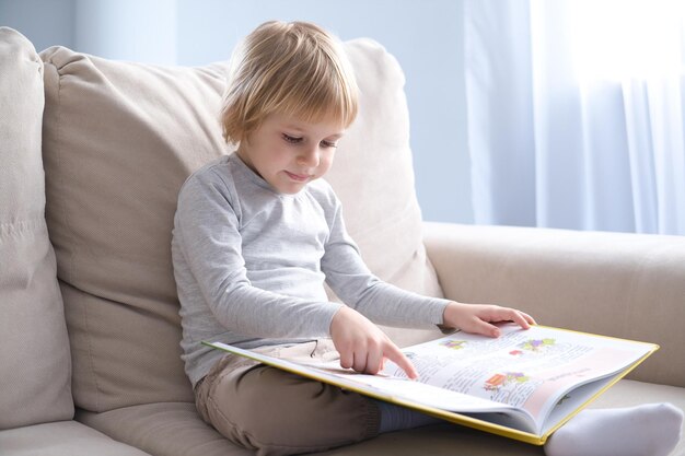 Photo little boy reading book sitting on sofa at home