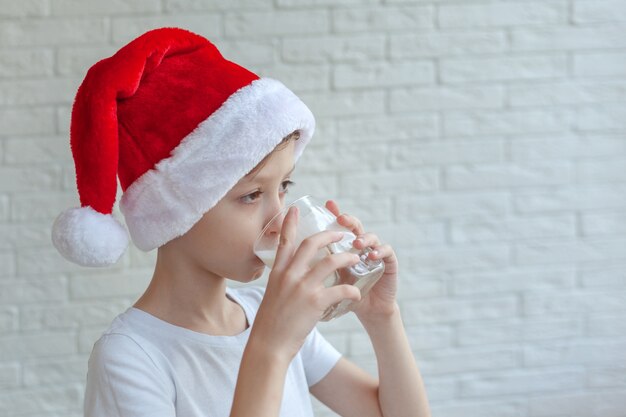 Little boy in red santa hat drinks milk