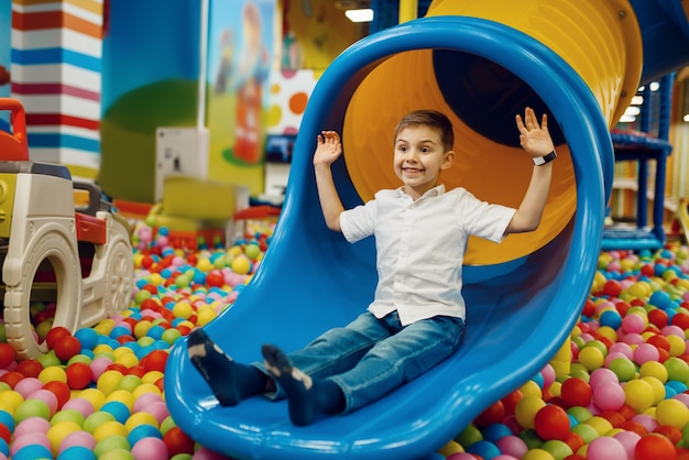 Photo little boy ride down the hill in the entertainment center. male child leisures on holidays, childhood happiness, happy kid on playground