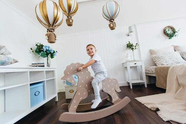 A little boy rides a rocking horse in a children's room Light interior