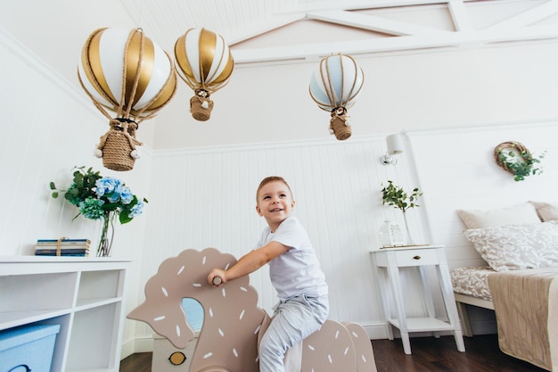 Photo a little boy rides a rocking horse in a children's room light interior