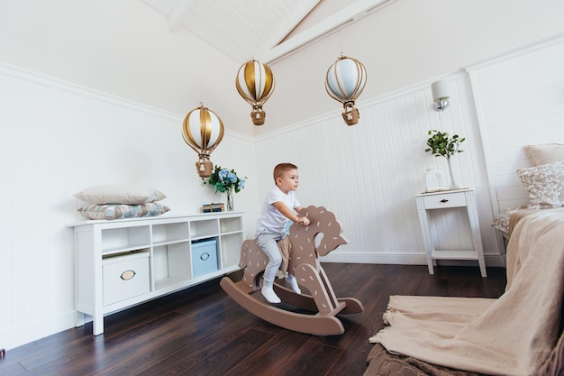 A little boy rides a rocking horse in a children's room Light interior