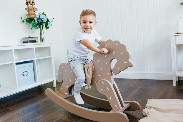 Un ragazzino cavalca un cavallo a dondolo in una stanza per bambini interni chiari