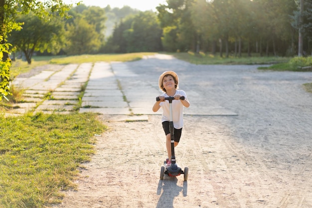Il ragazzino guida uno scooter in una soleggiata giornata estiva attività all'aperto per bambini sport attivo per bambini in età prescolare bambino su scooter da calcio nel parco