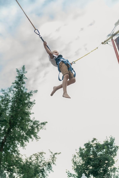 Little boy rides trampoline in an amusement park and jumps high into sky Child has fun in the theme park