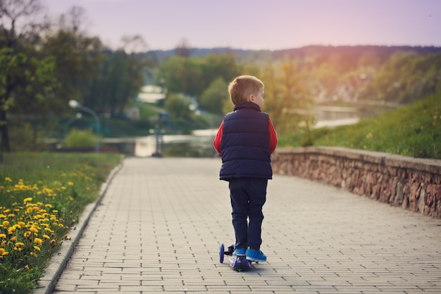 Photo little  boy riding and his scooter bicycle in summer, outdoors